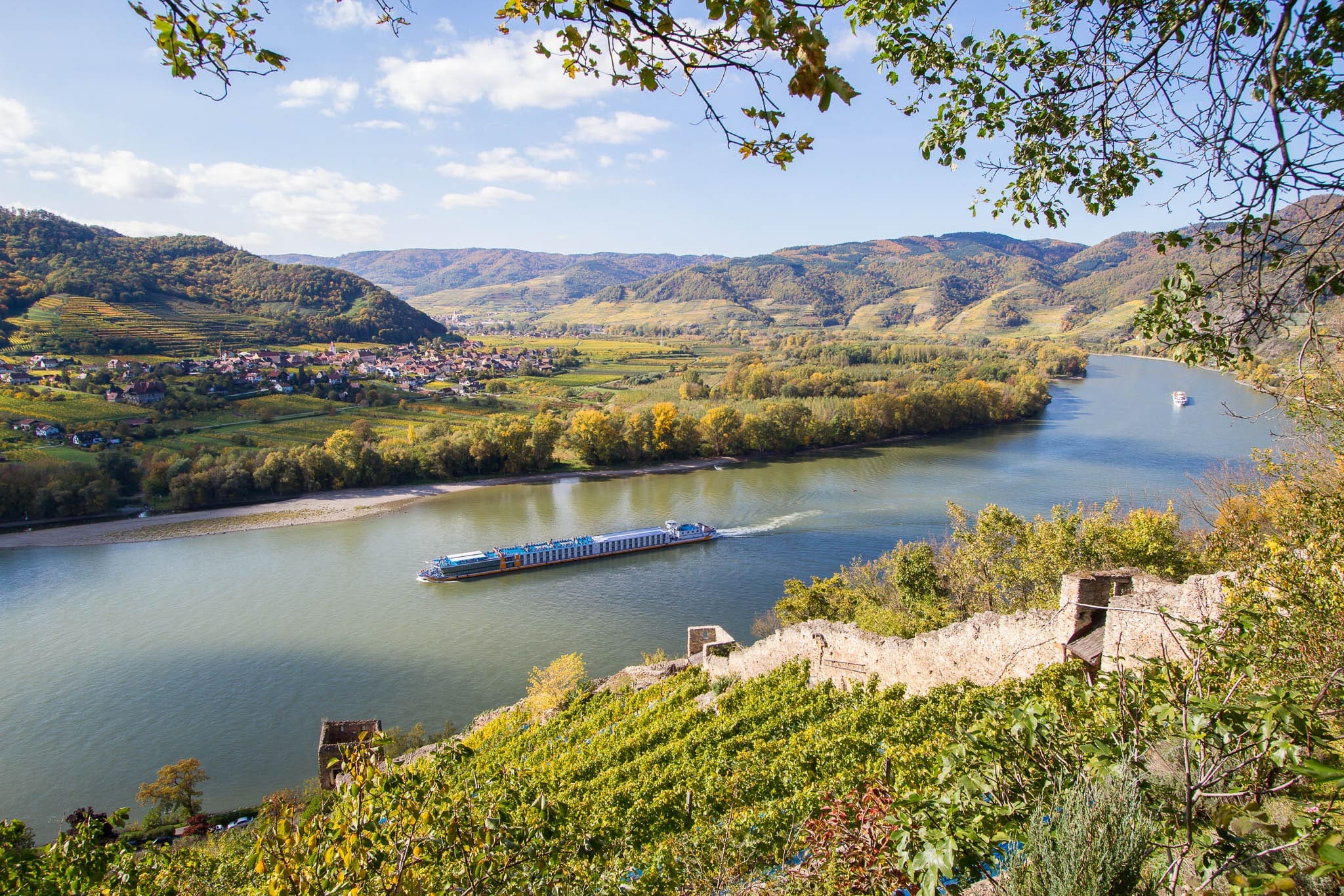 Scenic river cruise sailing through the Wachau Valley, surrounded by vineyards, rolling hills, and historic castles along the Danube River in Austria.