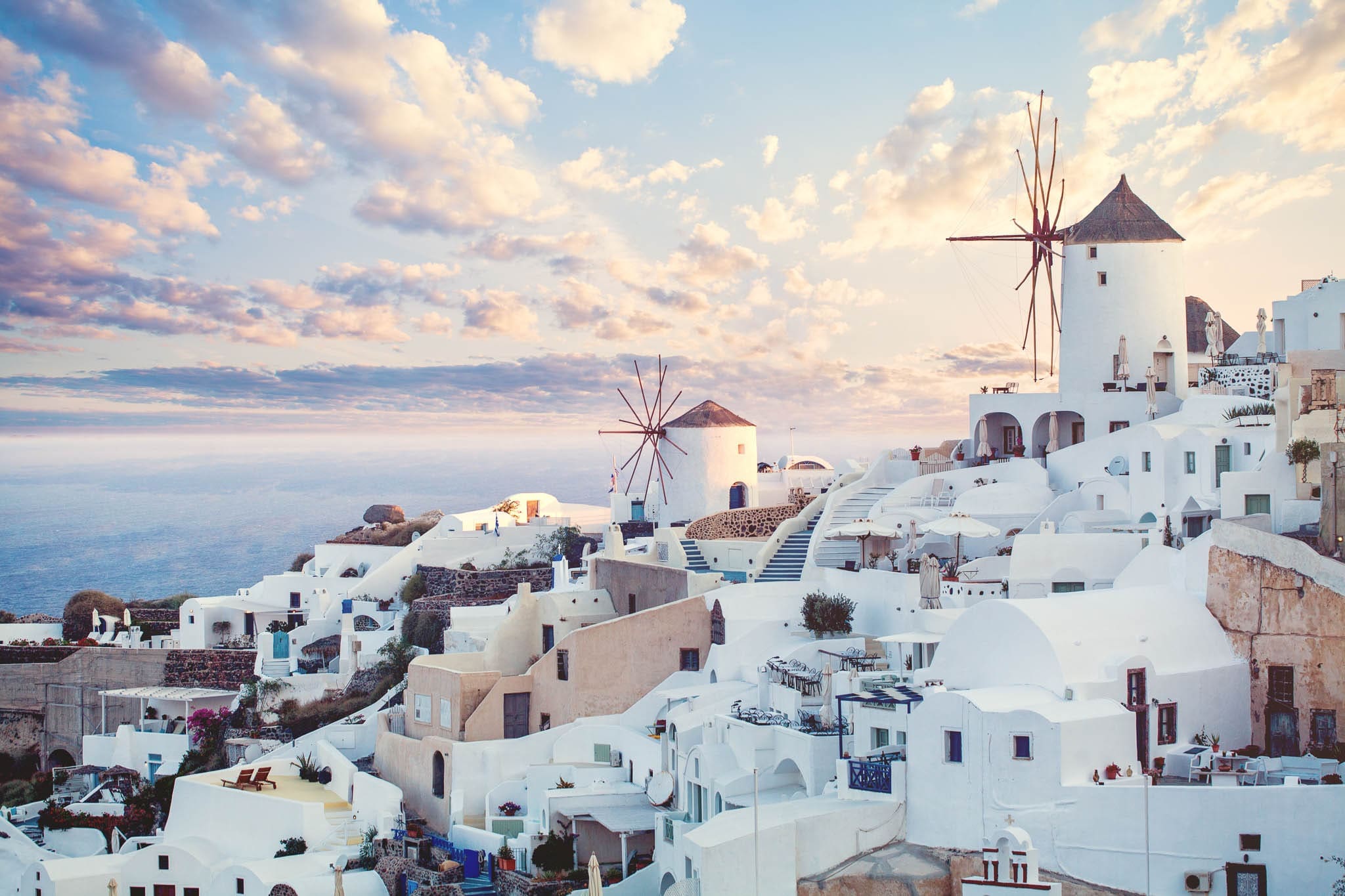 Whitewashed buildings and iconic windmills overlooking Santorini, Greece, at sunset.
